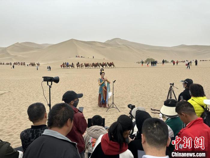 圖為2023年4月底，敦煌大漠“逐舞者”奧楠在鳴沙山月牙泉景區(qū)視頻直播，吸引游人圍觀?！●T志軍 攝